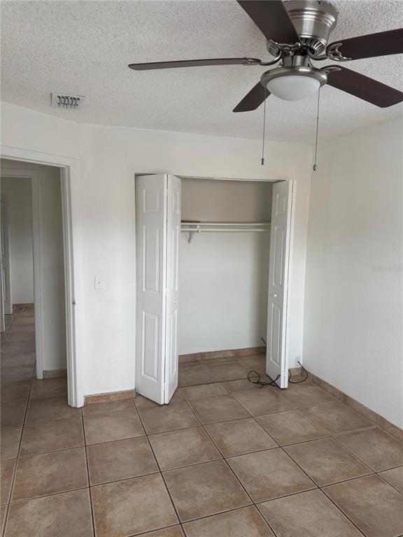 A bedroom with tile flooring, a ceiling fan, and an open closet with bi-fold doors — 712 MICHIGAN CT UNIT 3, ST CLOUD, FL