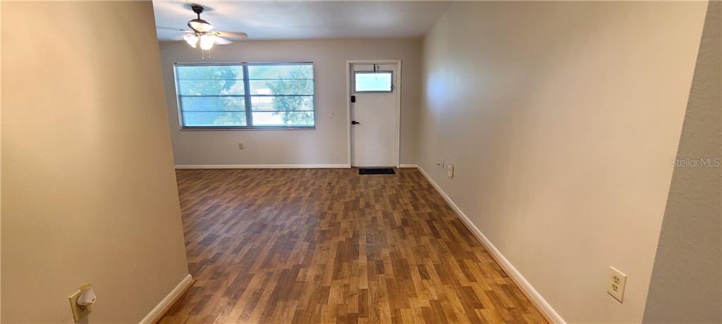 An empty room features light-colored walls, wood-look flooring, a ceiling fan, and a white door — 911 WASHINGTON AVENUE UNIT 305, LARGO, FL