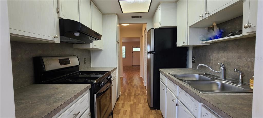 A galley kitchen features white cabinets, laminate countertops, a black stove, and a stainless refrigerator — 911 WASHINGTON AVENUE UNIT 305, LARGO, FL