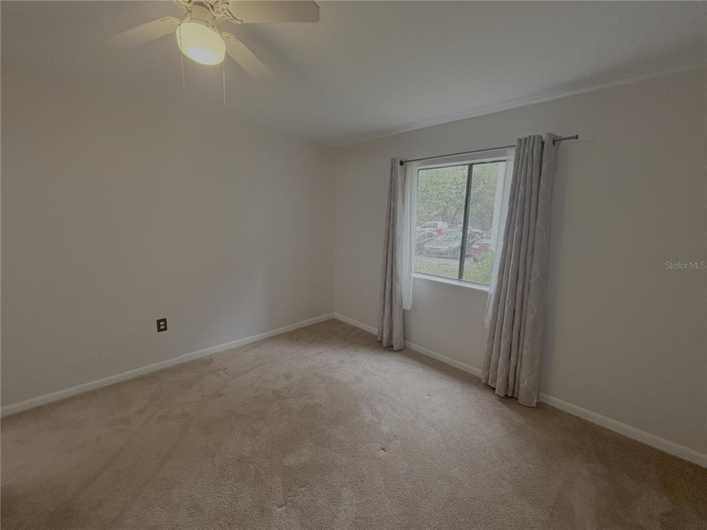 An empty bedroom features beige carpet, light-colored walls, a ceiling fan, and a window with curtains — 81 SE 16TH AVENUE UNIT D-103, GAINESVILLE, FL