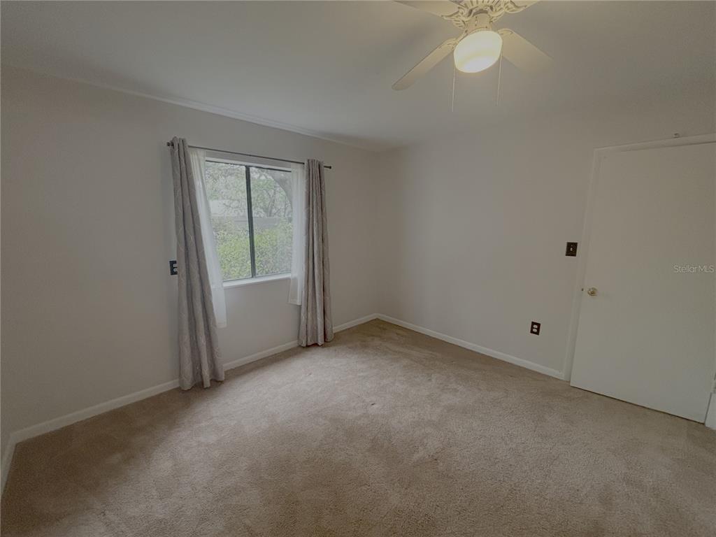 An empty bedroom features beige carpet, light gray walls, a ceiling fan, and a window — 81 SE 16TH AVENUE UNIT D-103, GAINESVILLE, FL