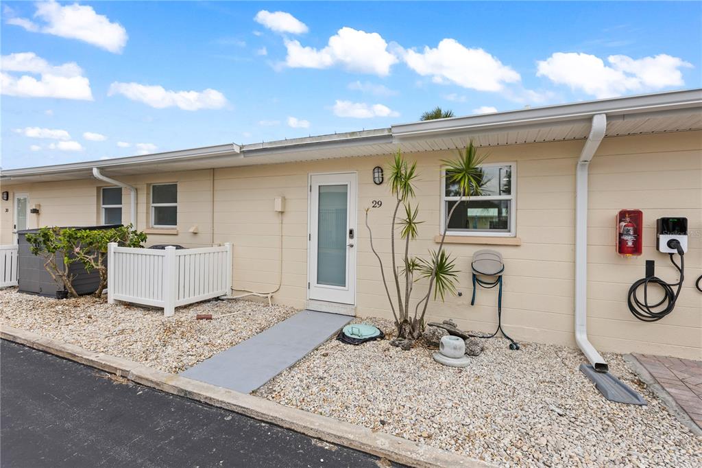 A single-story beige unit with a white front door, gravel yard, and EV charger — 5830 MIDNIGHT PASS ROAD UNIT 29, SARASOTA, FL