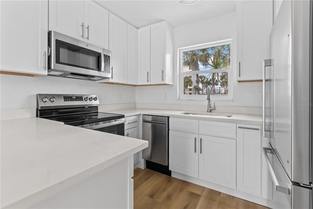 A kitchen features white cabinets, stainless steel appliances, white countertops, and light wood flooring — 5830 MIDNIGHT PASS ROAD UNIT 29, SARASOTA, FL