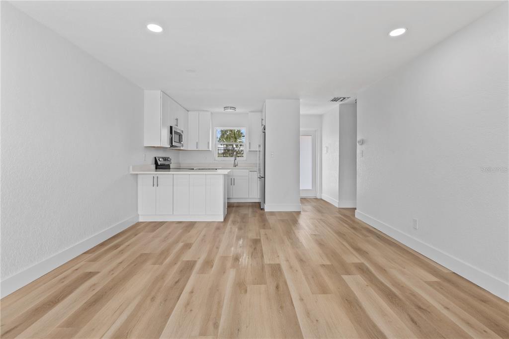 A bright kitchen with white cabinets and light wood flooring opens into a living area — 5830 MIDNIGHT PASS ROAD UNIT 29, SARASOTA, FL