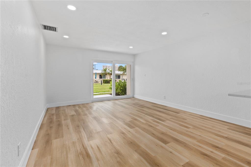 An empty room with light wood-look flooring, white walls, recessed lighting, and a sliding glass door — 5830 MIDNIGHT PASS ROAD UNIT 29, SARASOTA, FL