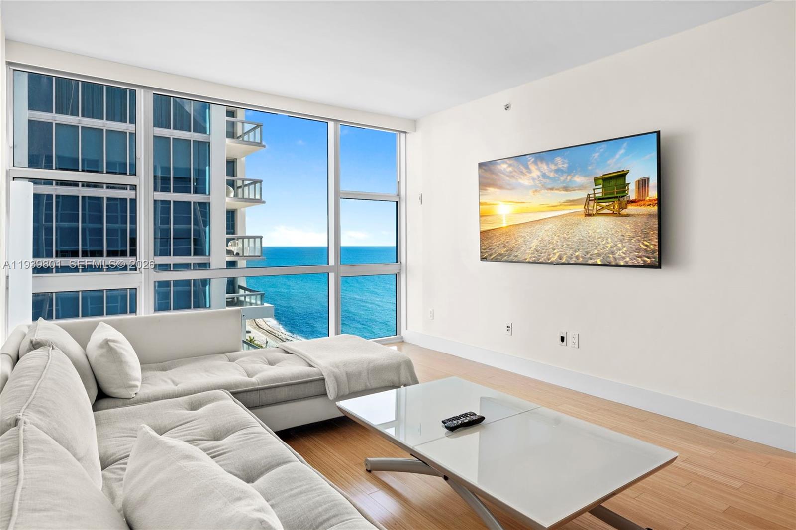 A living room features a white sectional sofa, glass coffee table, and ocean views — 6801 Collins Ave, Miami Beach FL 33141, MIAMI BEACH, FL