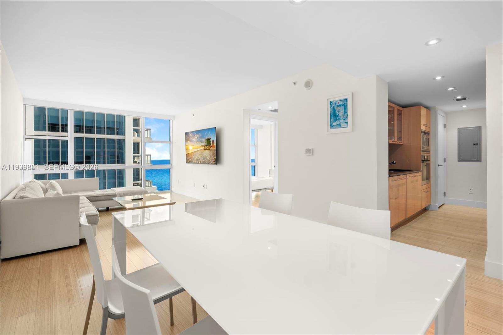 A bright, modern living and dining area features white furniture, light wood floors, and ocean views — 6801 Collins Ave, Miami Beach FL 33141, MIAMI BEACH, FL