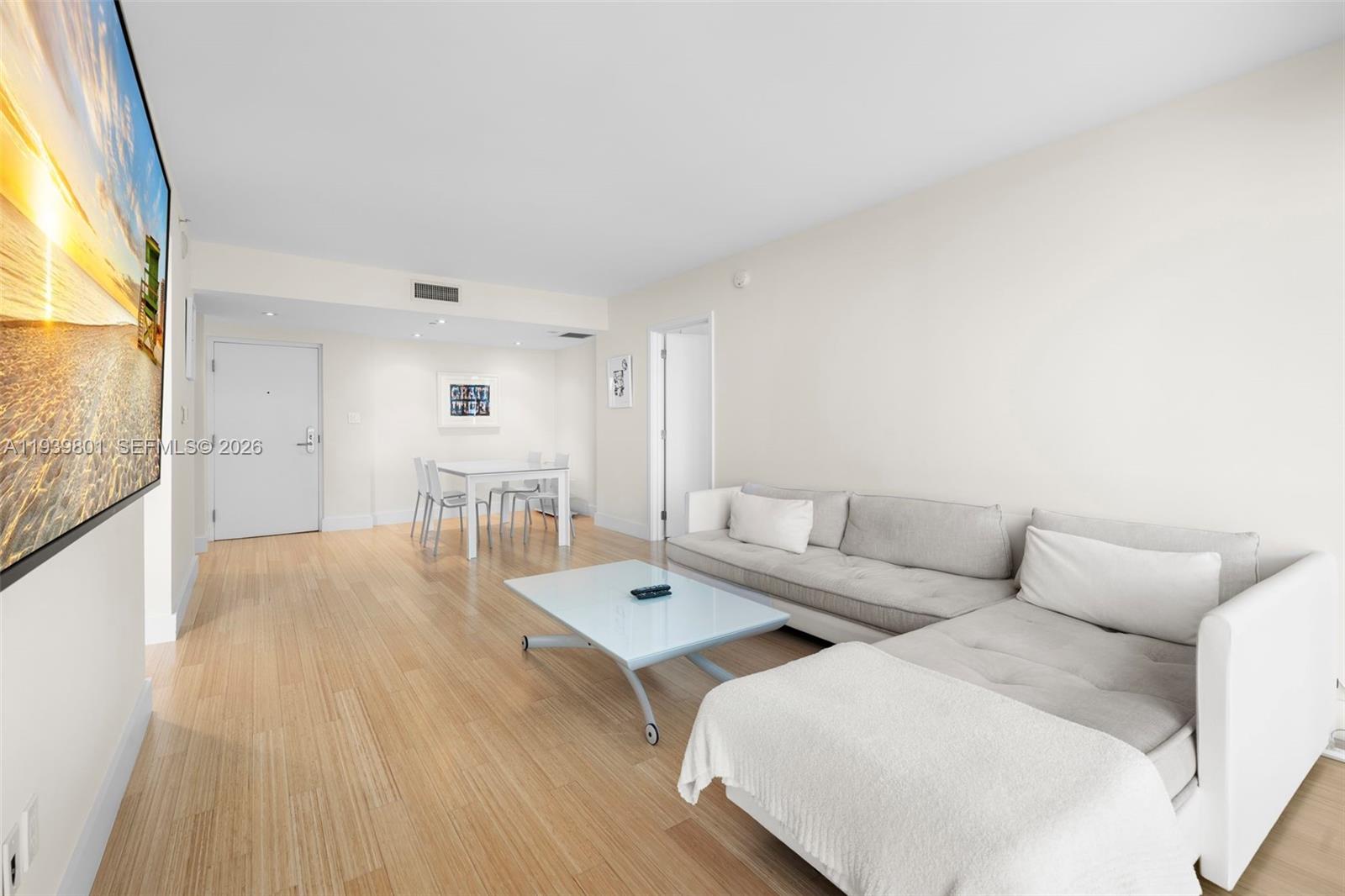 A living room features light wood flooring, a sectional sofa, and a dining area — 6801 Collins Ave, Miami Beach FL 33141, MIAMI BEACH, FL