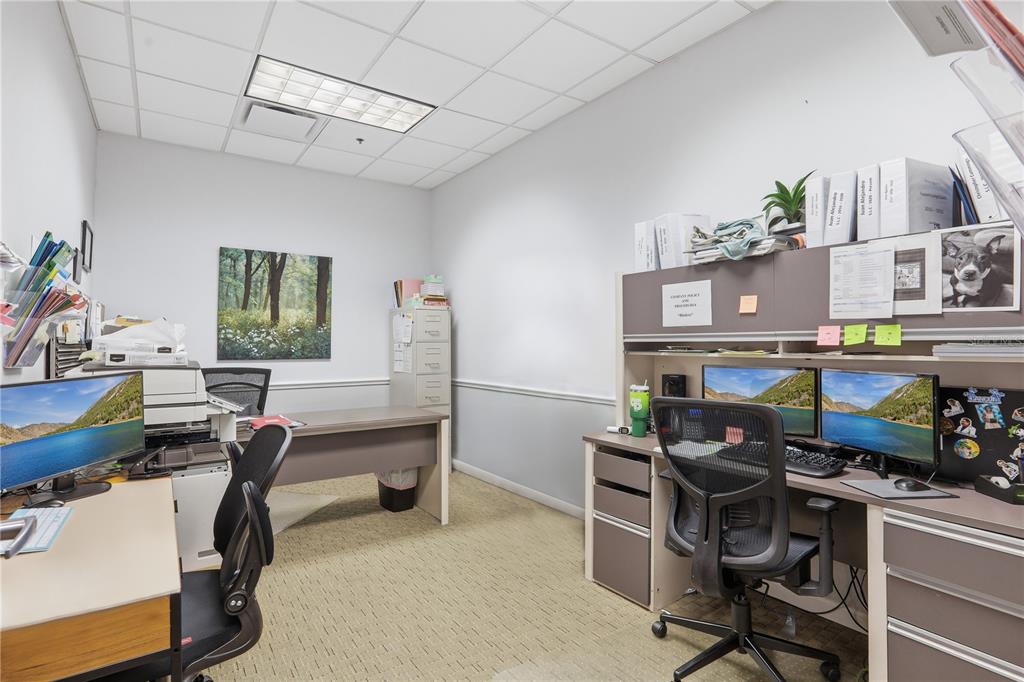 An office space features two desks, dual computer monitors, a filing cabinet, and carpeted flooring — 10967 LAKE UNDERHILL ROAD UNIT 112, ORLANDO, FL