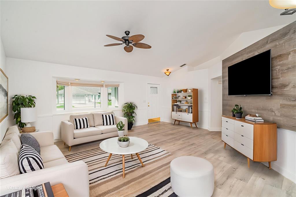 A living room features a wood-paneled accent wall, light flooring, and a ceiling fan — 2048 BERRY ROBERTS DRIVE, SUN CITY CENTER, FL