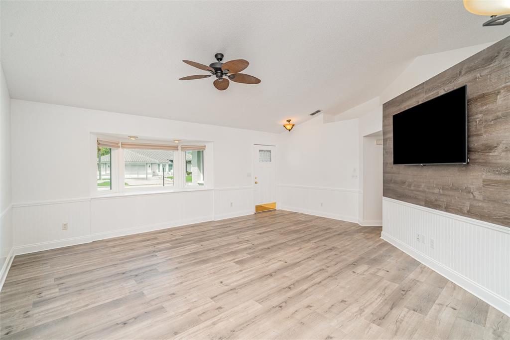 A living room features light wood-look flooring, white wainscoting, a bay window, and a television — 2048 BERRY ROBERTS DRIVE, SUN CITY CENTER, FL