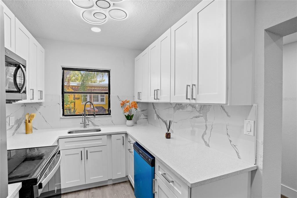 A white kitchen features marble-style backsplashes, shaker cabinets, and a blue-covered dishwasher — 630 180TH AVENUE E, REDINGTON SHORES, FL