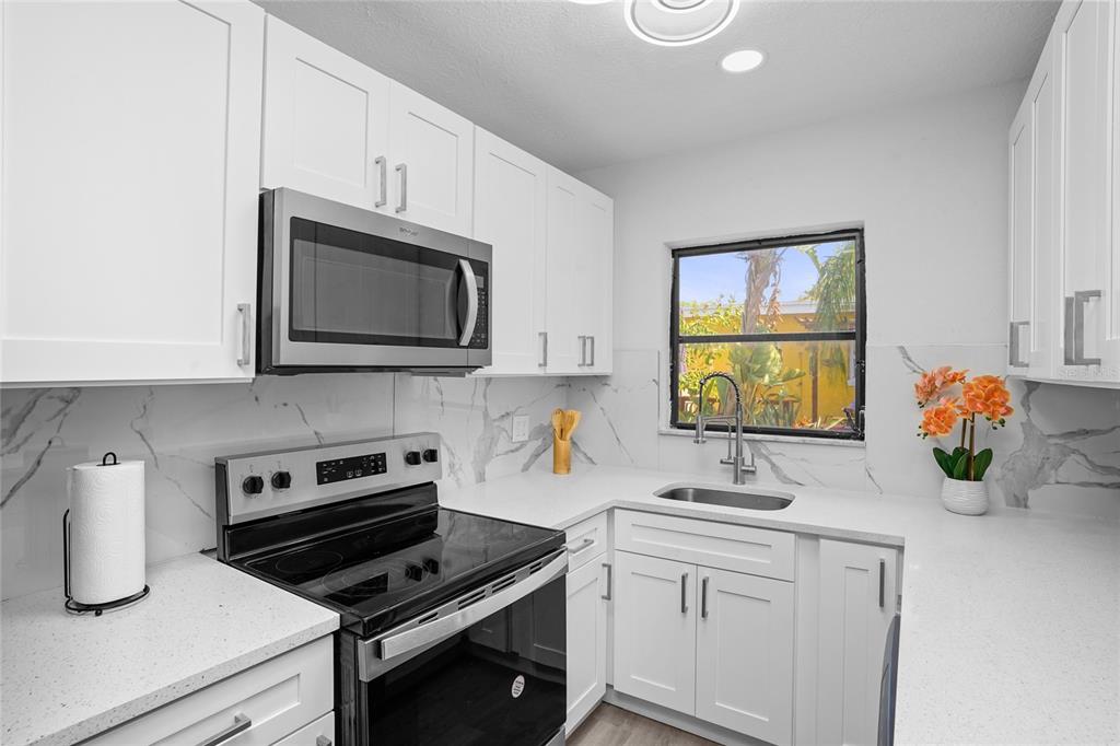 A white kitchen features stainless steel appliances, quartz countertops, and a marble-patterned backsplash — 630 180TH AVENUE E, REDINGTON SHORES, FL