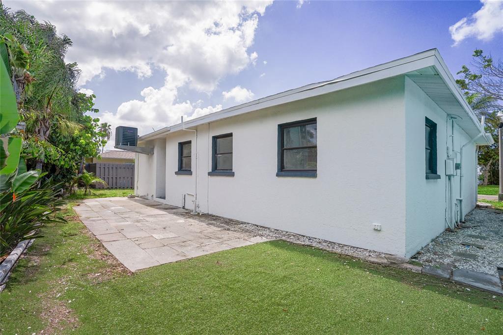 A white exterior wall of a house features dark-framed windows, a patio, and artificial turf — 630 180TH AVENUE E, REDINGTON SHORES, FL