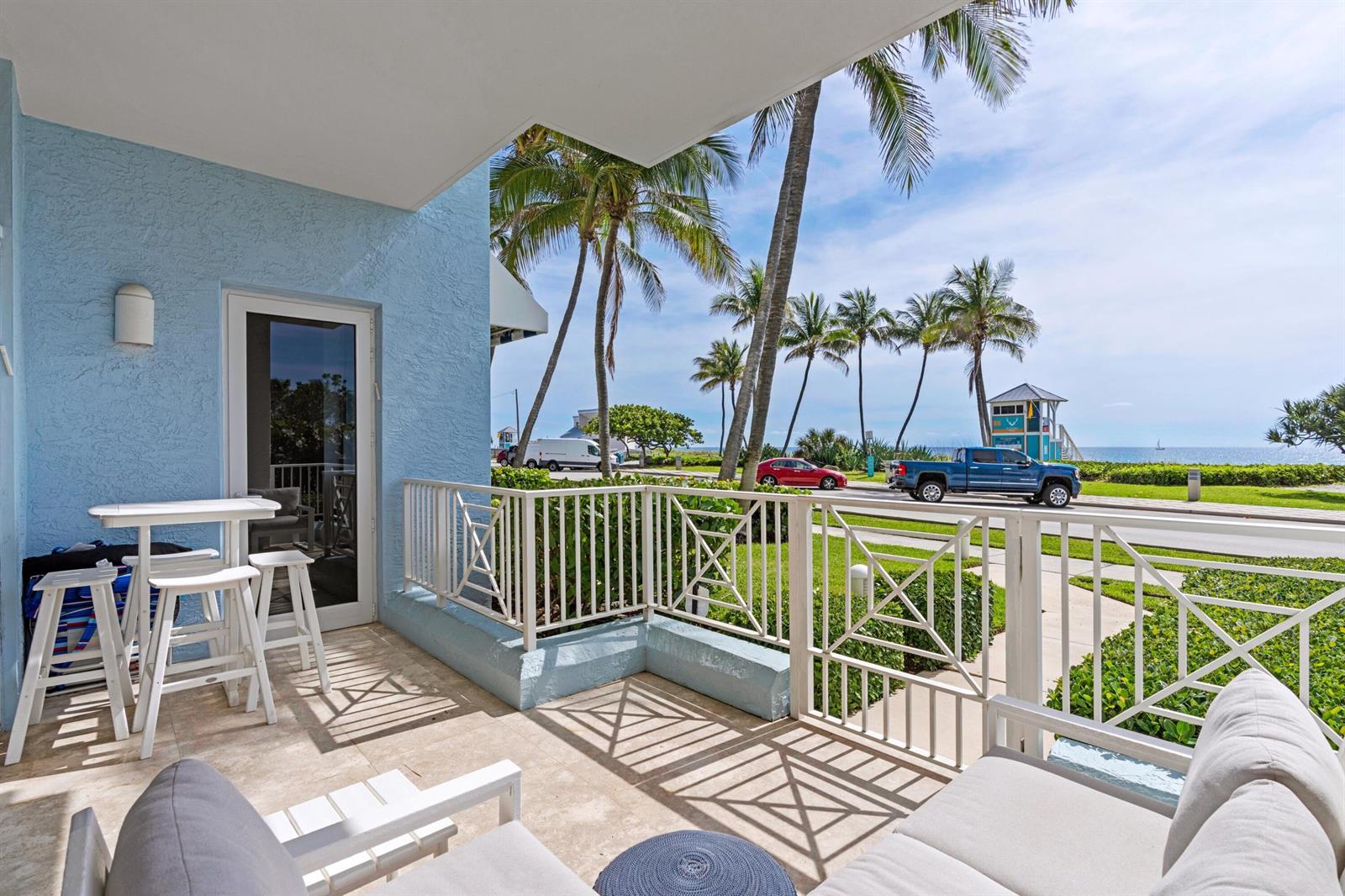 A balcony with white furniture overlooks a street, palm trees, and the ocean — 701 SE 21st Avenue # 109, Deerfield Beach FL 33441, DEERFIELD BEACH, FL