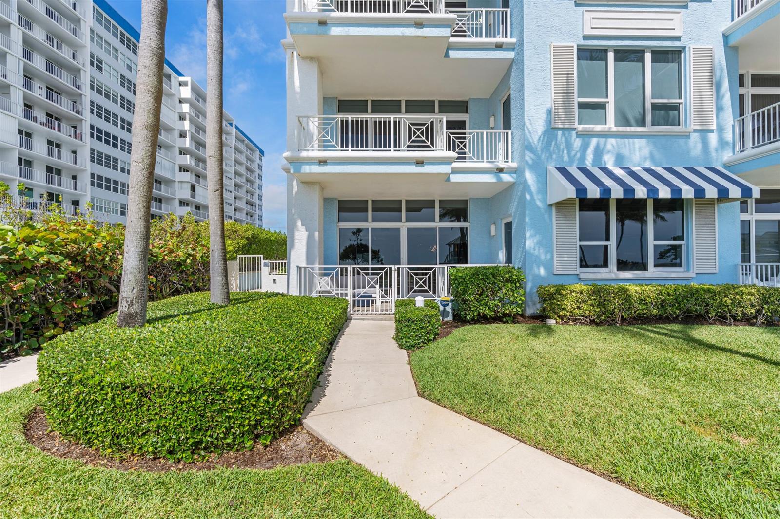A blue multi-story building exterior features a ground-level patio, a walkway, and manicured landscaping — 701 SE 21st Avenue # 109, Deerfield Beach FL 33441, DEERFIELD BEACH, FL