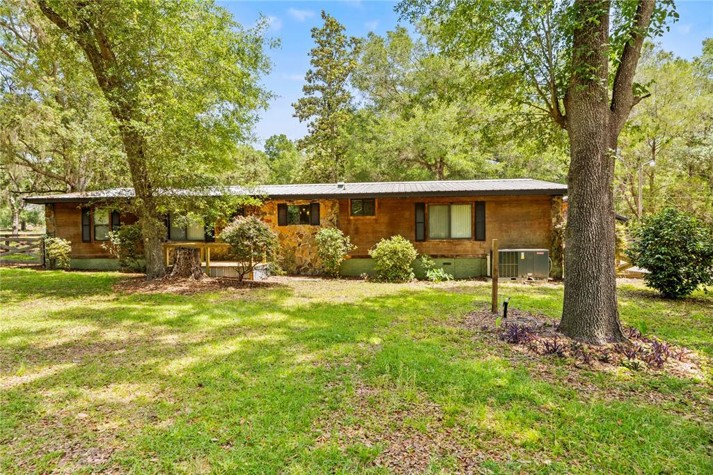 A single-story house with wood siding and a stone facade sits in a wooded yard — 27137 LAMBETH ROAD, BROOKSVILLE, FL