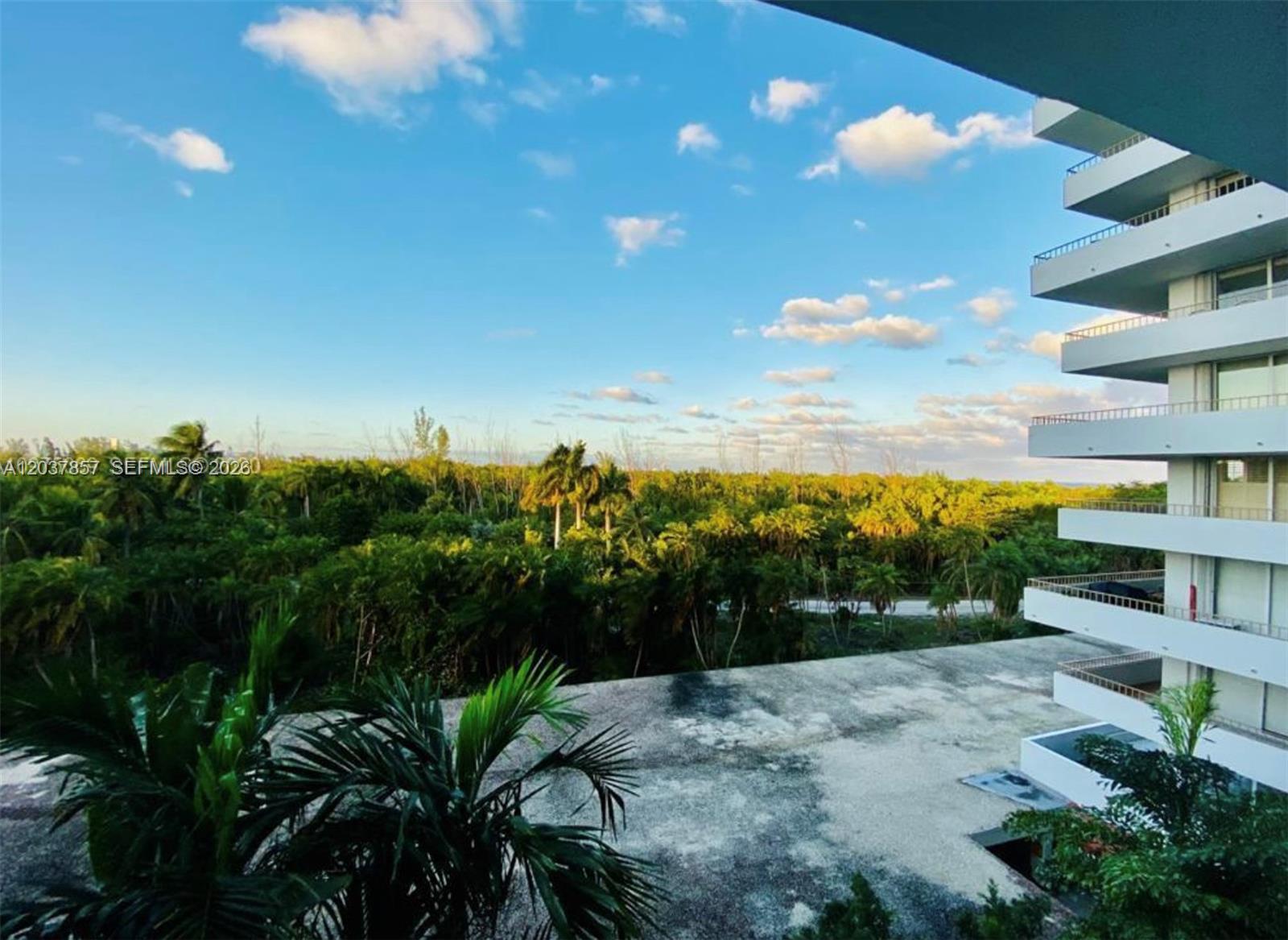 An empty living room features light wood-look flooring, white walls, and a sliding glass balcony door — 155 Ocean Lane Dr # 504, Key Biscayne FL 33149, KEY BISCAYNE, FL