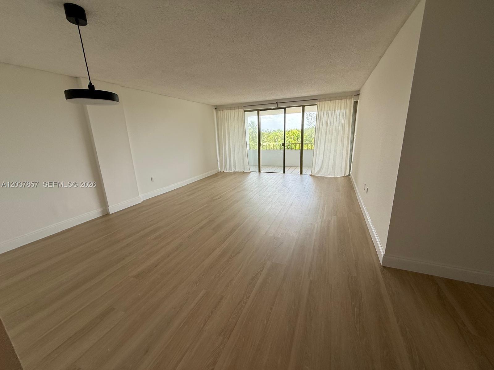 An empty room features light wood-look flooring, white walls, a pendant light, and a balcony — 155 Ocean Lane Dr # 504, Key Biscayne FL 33149, KEY BISCAYNE, FL
