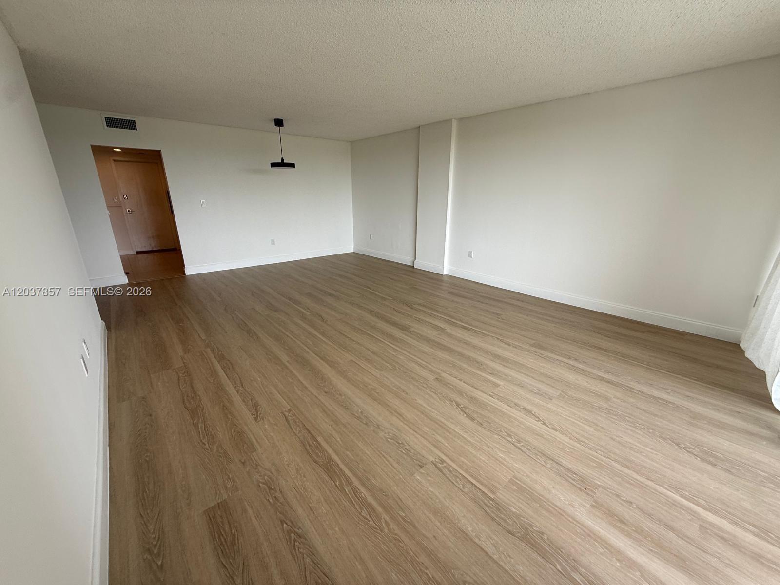 An empty room features light wood-look flooring, white walls, and a single hanging light fixture — 155 Ocean Lane Dr # 504, Key Biscayne FL 33149, KEY BISCAYNE, FL
