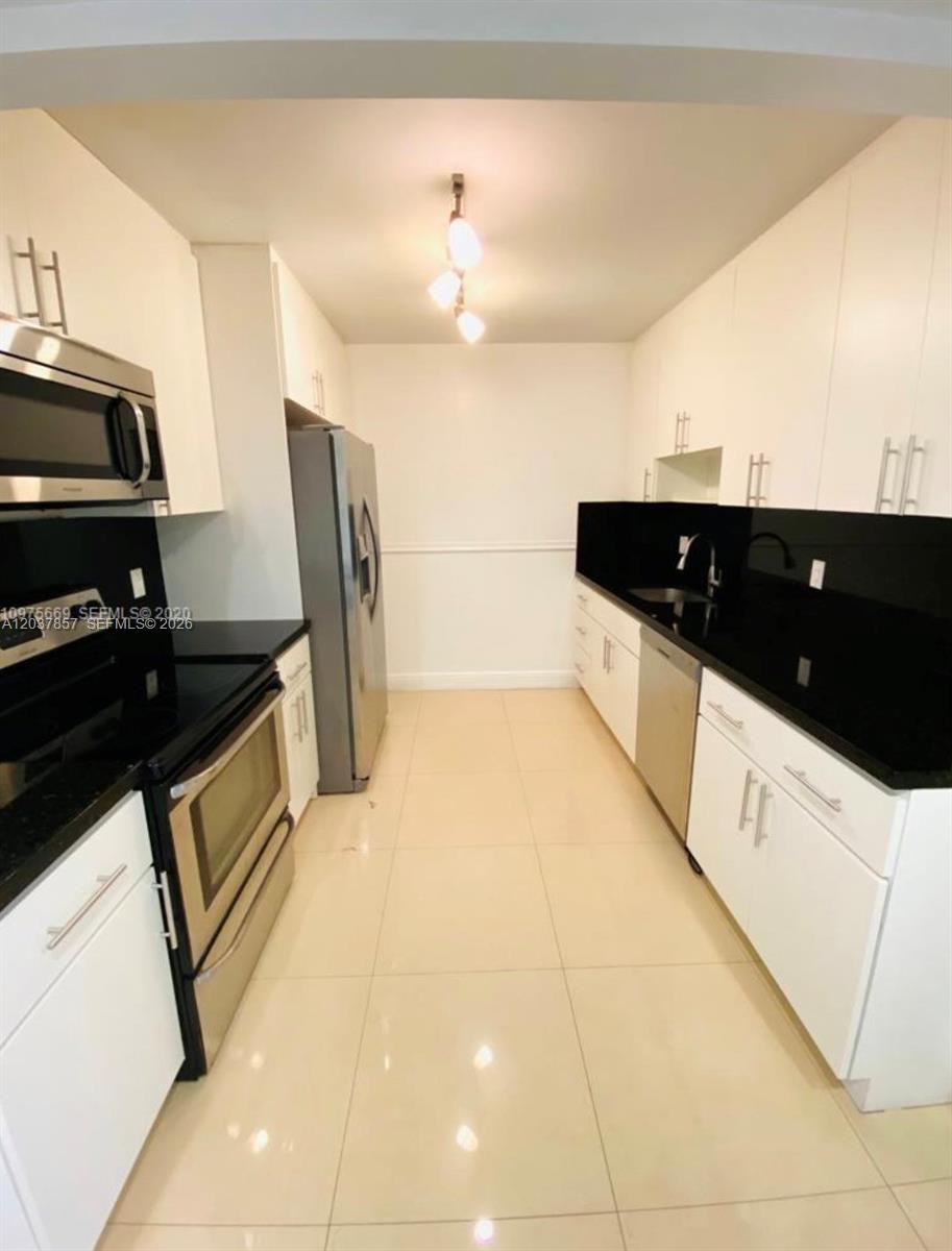 This galley kitchen features white cabinets, black countertops, stainless steel appliances, and tile flooring — 155 Ocean Lane Dr # 504, Key Biscayne FL 33149, KEY BISCAYNE, FL