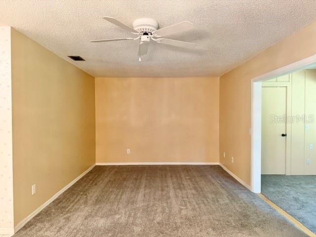 An empty room with beige walls, gray carpeting, and a white ceiling fan — 101 GRAND PLAZA DRIVE UNIT F4, ORANGE CITY, FL