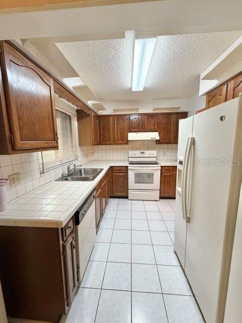 A kitchen features wood cabinets, white tile countertops, white appliances, and white floor tiles — 101 GRAND PLAZA DRIVE UNIT F4, ORANGE CITY, FL