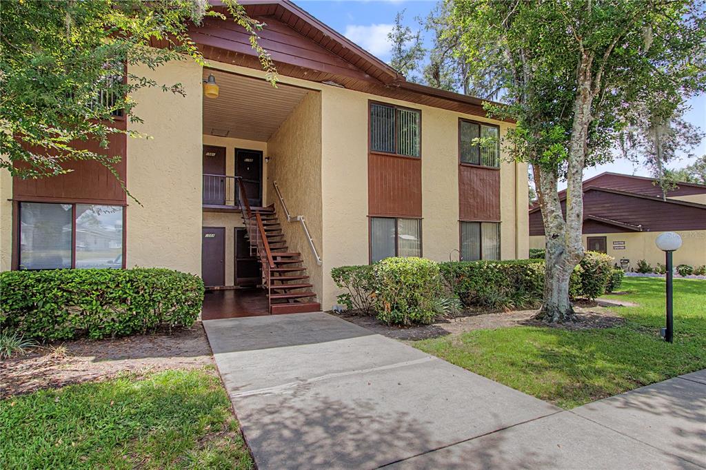 A two-story apartment building exterior features a concrete walkway, wooden stairs, and tan stucco walls — 510 SILVER COURSE UNIT B, OCALA, FL