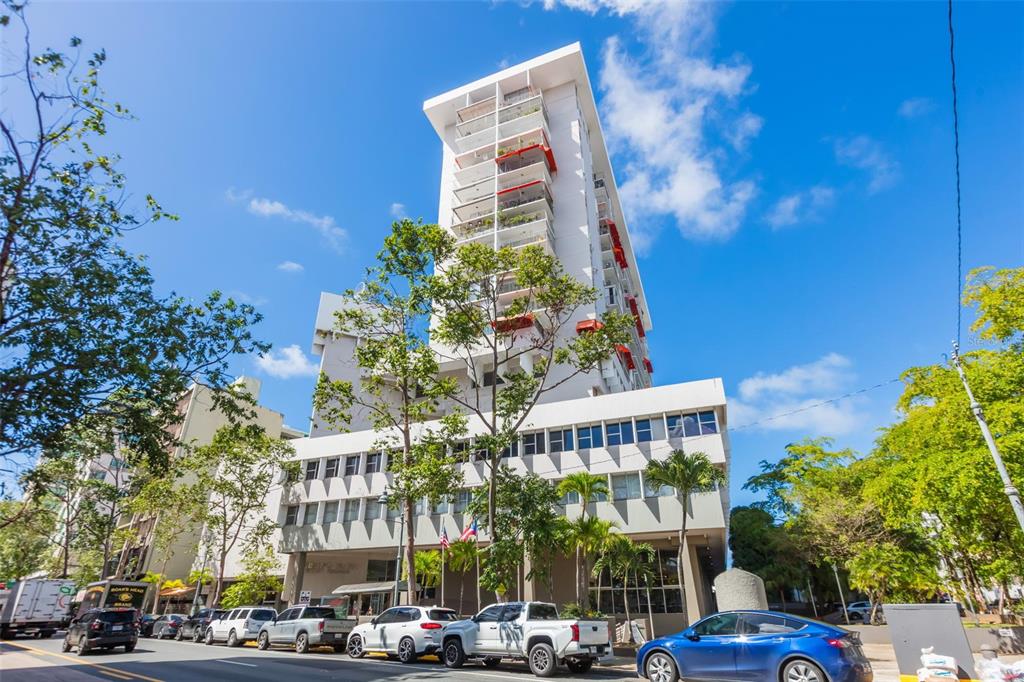 A multi-story white apartment building stands above a street with parked cars and trees — C. Bolivar COBIANS PLAZA AVENUE UNIT 21, SAN JUAN, PR