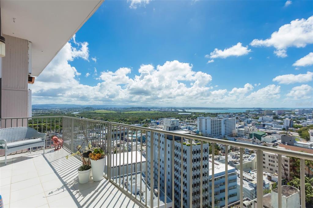 A high-rise balcony with a white bench, potted plants, and a panoramic city and water view — C. Bolivar COBIANS PLAZA AVENUE UNIT 21, SAN JUAN, PR