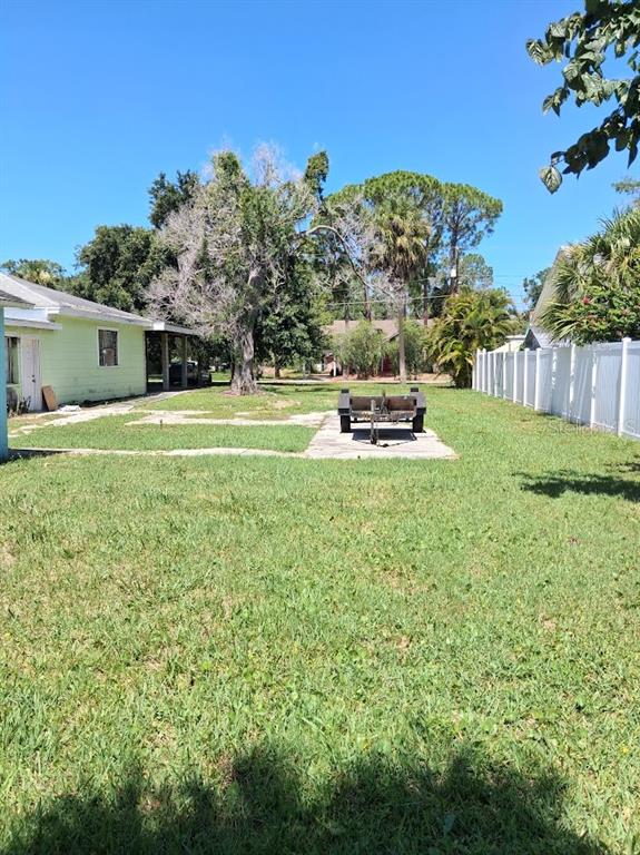 A grassy backyard features a concrete pad with a small utility trailer and a fence — BANANA STREET, TARPON SPRINGS, FL
