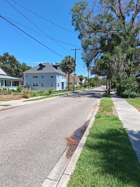 A street view showing a light blue house, a sidewalk, and large trees under blue skies — BANANA STREET, TARPON SPRINGS, FL