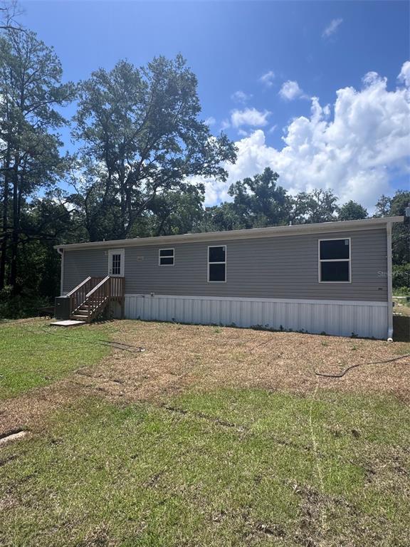 The exterior of a gray manufactured home features white skirting and a wooden staircase — 11801 NW 20TH STREET, OCALA, FL