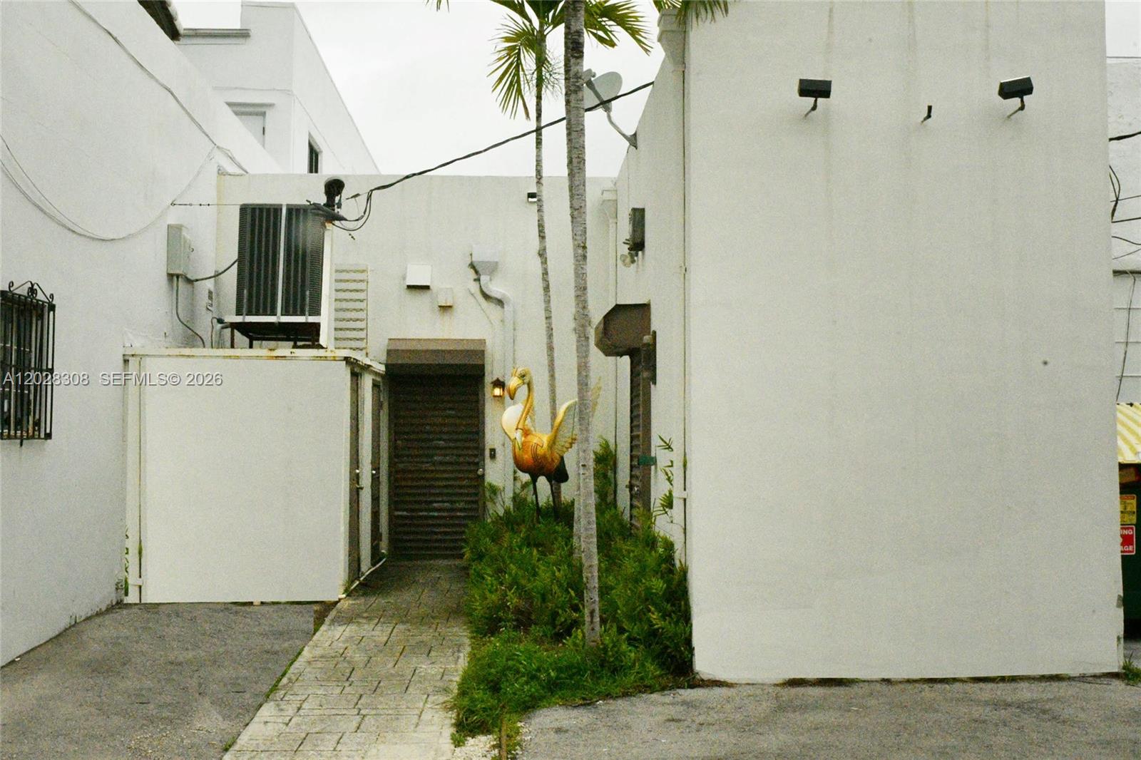 A paved walkway leads to a building entrance featuring a golden flamingo statue and palm trees — 314 Coral Way, Coral Gables FL 33134, CORAL GABLES, FL