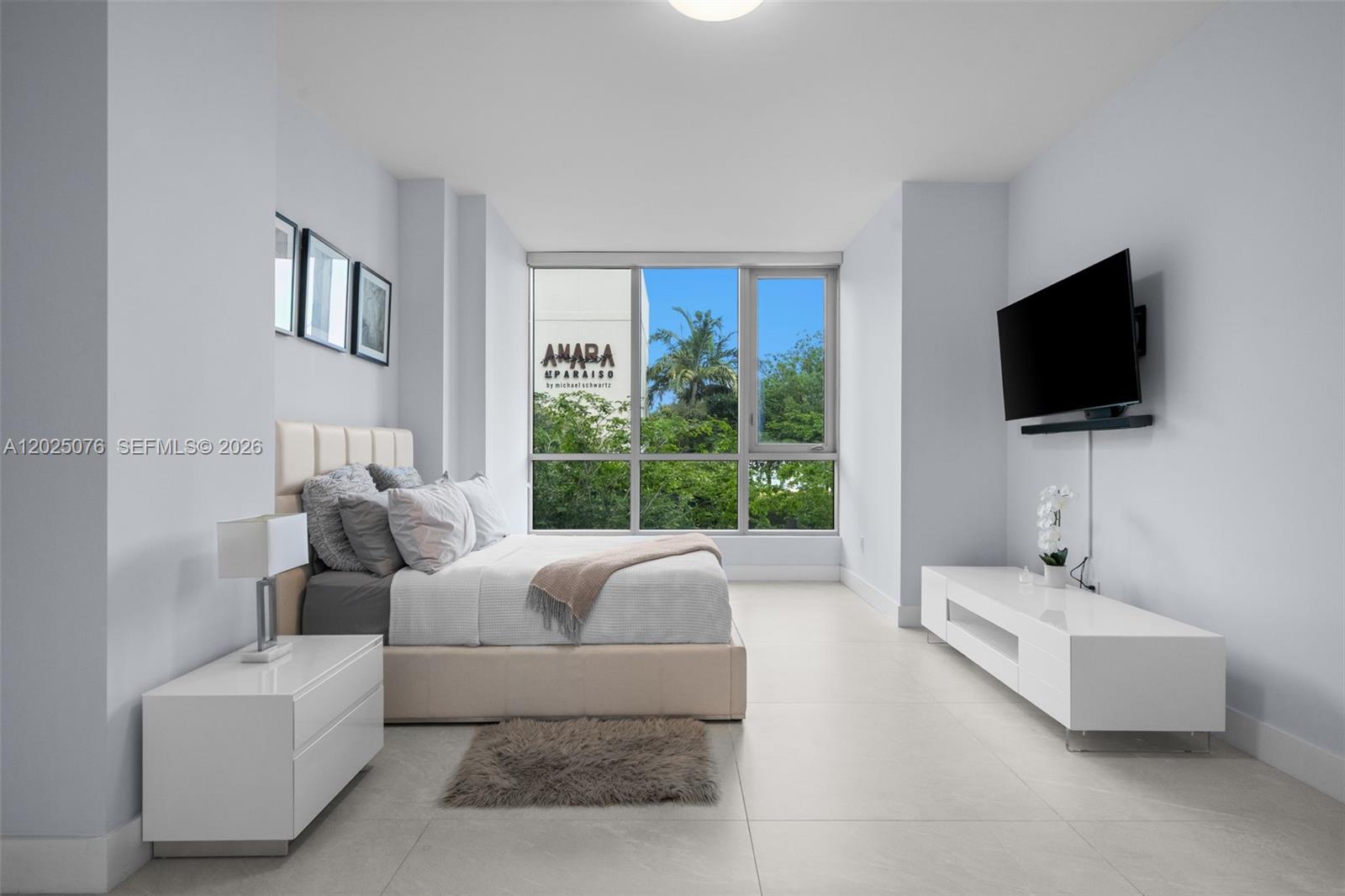 A modern bedroom features a bed, white furniture, a wall-mounted television, and floor-to-ceiling windows — 650 NE 32nd St, Miami FL 33137, MIAMI, FL