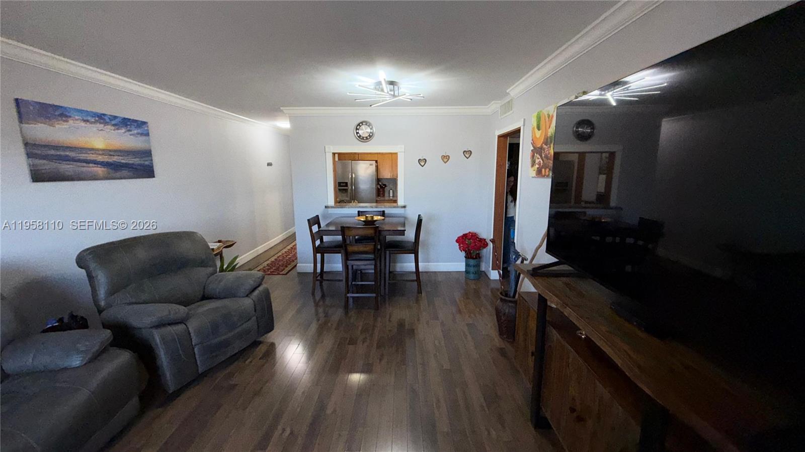 A living room features wood flooring, a gray recliner, a dining set, and a television — 1075 W 68th St # 403, Hialeah FL 33014, HIALEAH, FL