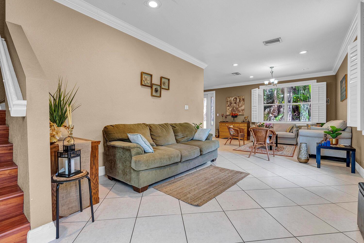 A living room with a green sofa, tiled floors, and a view into a dining area — 8020 NW 70th Avenue, Parkland FL 33067, PARKLAND, FL