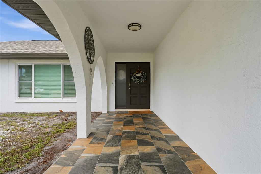 A covered entryway features a tiled floor, arched columns, and a dark front door — 6020 10TH AVENUE W, BRADENTON, FL