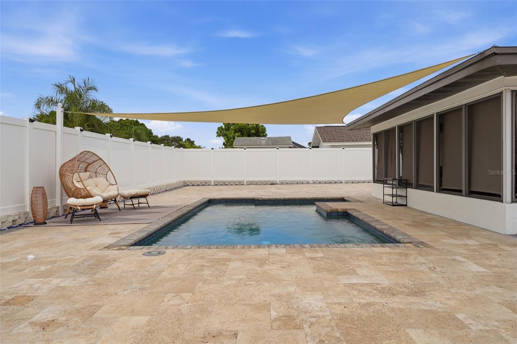 A backyard features a rectangular swimming pool, a tan shade sail, and a wicker chair — 6020 10TH AVENUE W, BRADENTON, FL