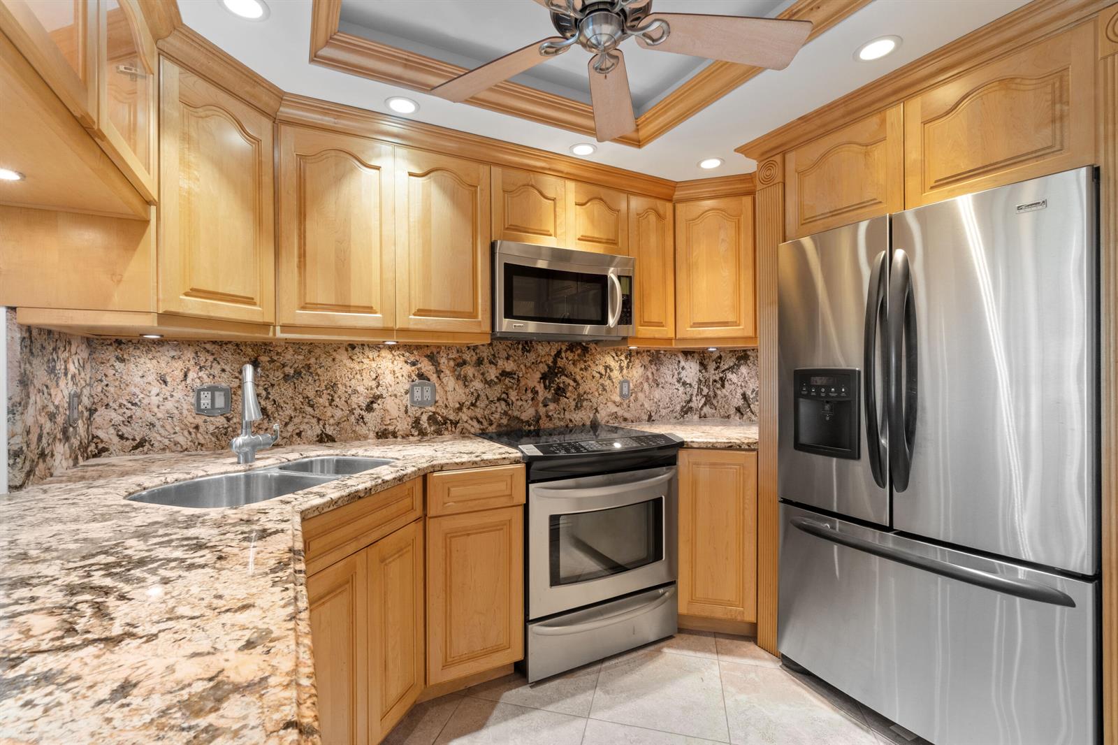 A kitchen features light wood cabinets, granite countertops, stainless steel appliances, and a ceiling fan — 2731 NE 14th St Causeway # 115, Pompano Beach FL 33062, POMPANO BEACH, FL