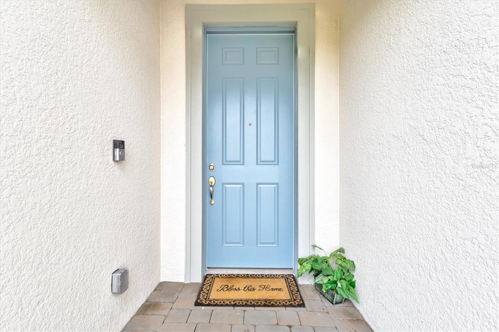 A light blue front door with a welcome mat sits in a white stucco entryway — 2534 GABEL OAK DRIVE, NORTH PORT, FL