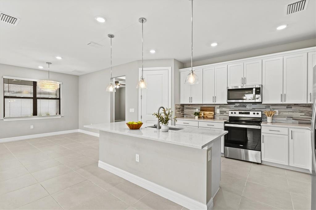 A modern kitchen features white cabinetry, a quartz-topped island, and stainless steel appliances — 2534 GABEL OAK DRIVE, NORTH PORT, FL