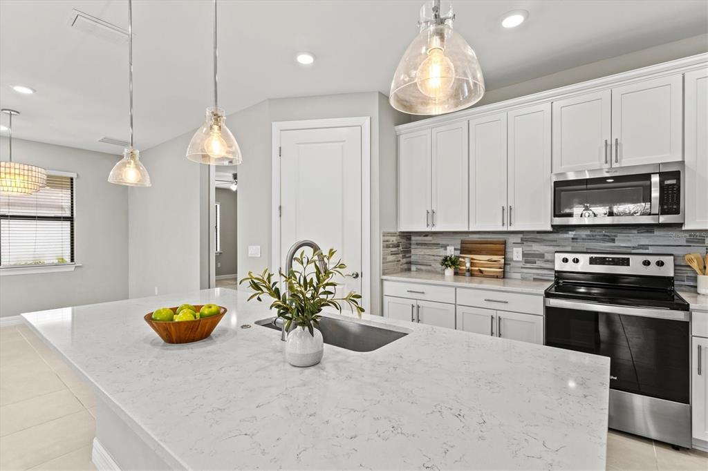 A modern kitchen features white cabinets, a quartz island with a sink, and stainless appliances — 2534 GABEL OAK DRIVE, NORTH PORT, FL
