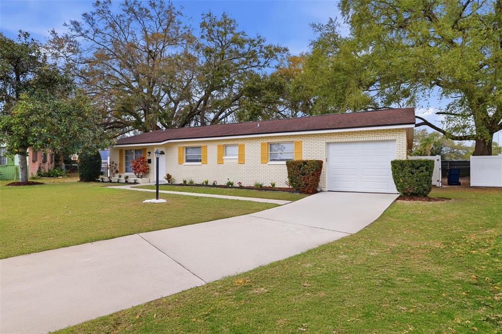 A single-story brick house with a white garage door and yellow shutters sits on grass — 2327 W KNOLLWOOD PLACE, TAMPA, FL