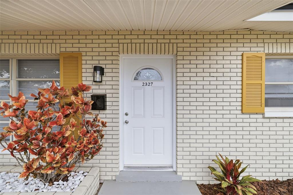 A white front door with a small arched window sits in a light brick wall — 2327 W KNOLLWOOD PLACE, TAMPA, FL