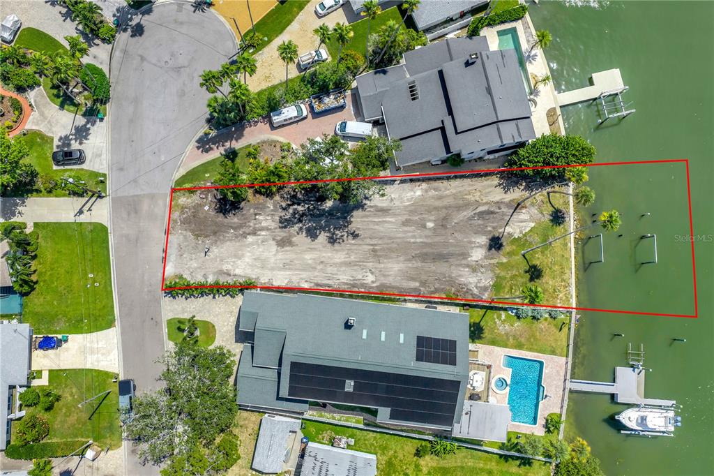 An aerial view shows a vacant, rectangular waterfront lot outlined in red between two houses — 315 10TH AVENUE, INDIAN ROCKS BEACH, FL
