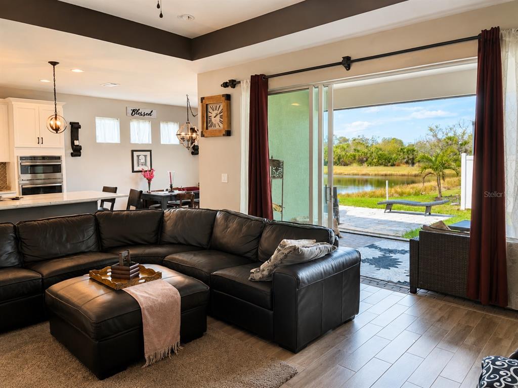 A living room with a black leather sectional sofa opens to a patio overlooking a pond — 12571 NIGHT VIEW DRIVE, SARASOTA, FL