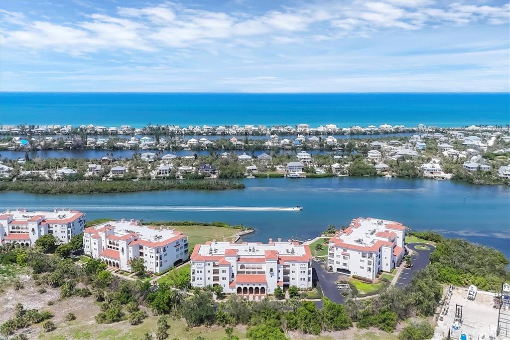 An aerial view shows waterfront apartment buildings with red roofs near a canal and ocean — 11100 HACIENDA DEL MAR BOULEVARD UNIT G-304, PLACIDA, FL