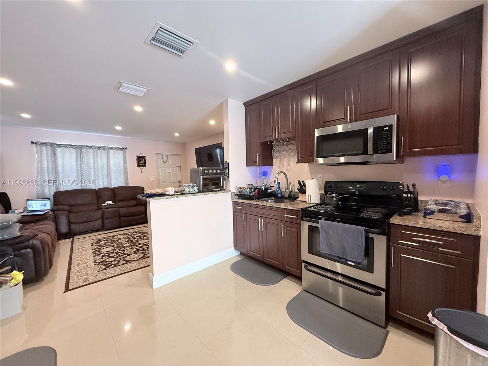 A kitchen with dark wood cabinets and stainless steel appliances opens into a living room — 1878 NW 45th Ct, Tamarac FL 33309, TAMARAC, FL