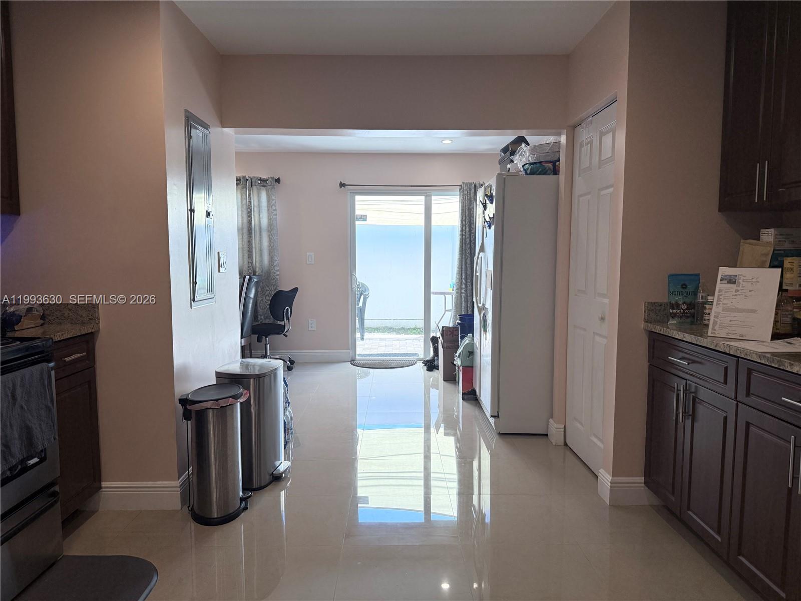 A kitchen with dark cabinets and tile flooring leads to a sliding glass door — 1878 NW 45th Ct, Tamarac FL 33309, TAMARAC, FL